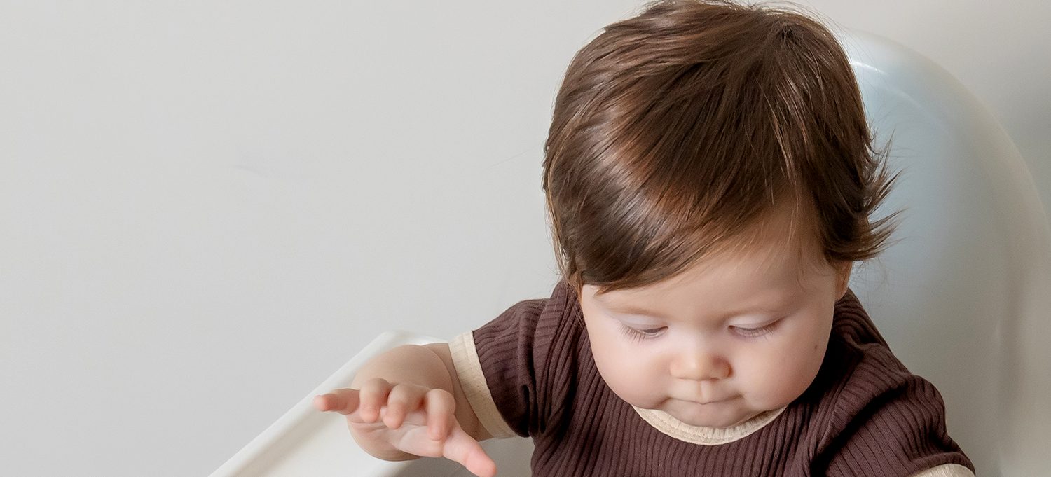 Baby self feeding from a SAMiGO silicone suction plate and bowl at the high chair